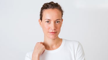 Eine junge Frau, bekleidet mit einem weißen T-Shirt schaut zufrieden in die Kamera